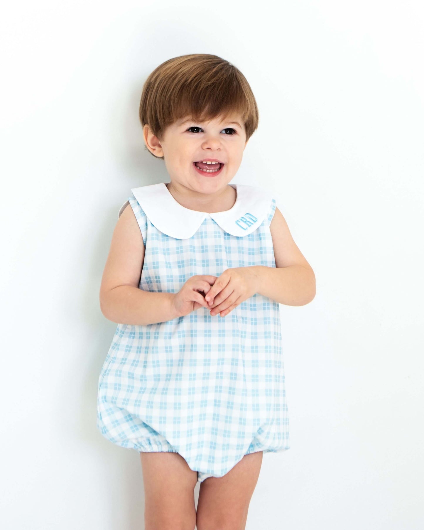 Child wearing a blue checkered dress with a white collar against a white background