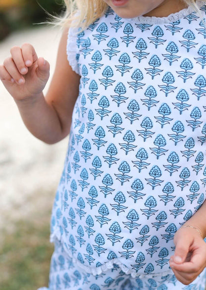 Child wearing a blue floral patterned set with a blurred natural background