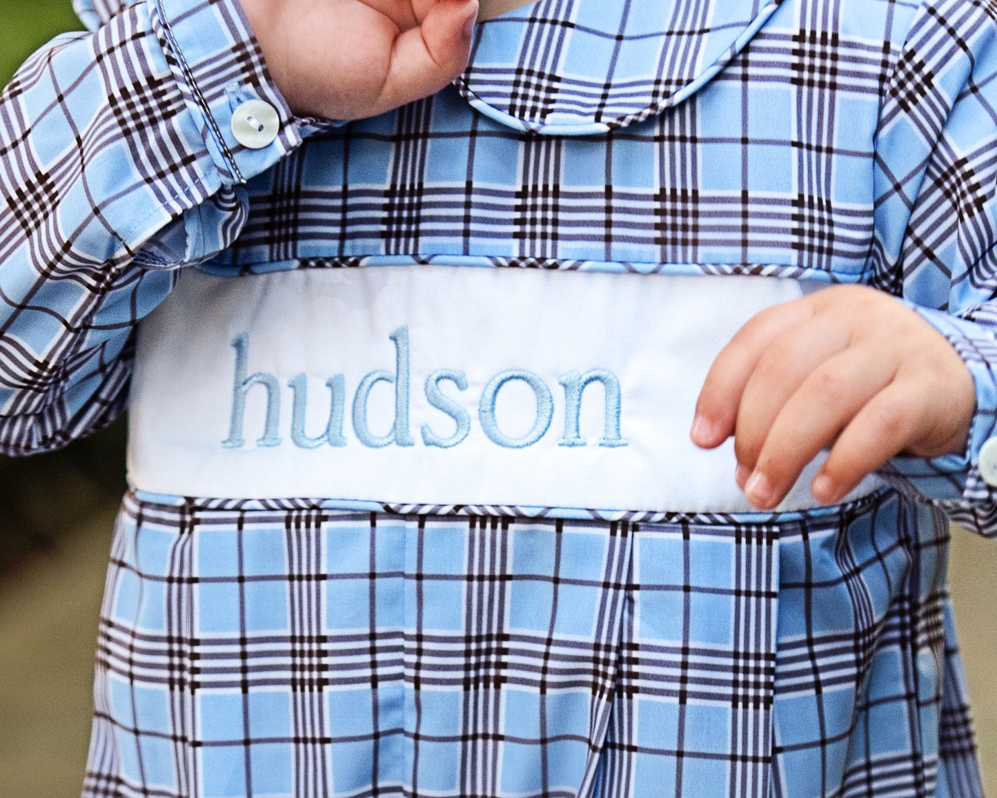 Child wearing a blue plaid outfit with 'hudson' embroidered on the chest.