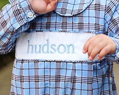 Child wearing a blue plaid outfit with 'hudson' embroidered on the chest.