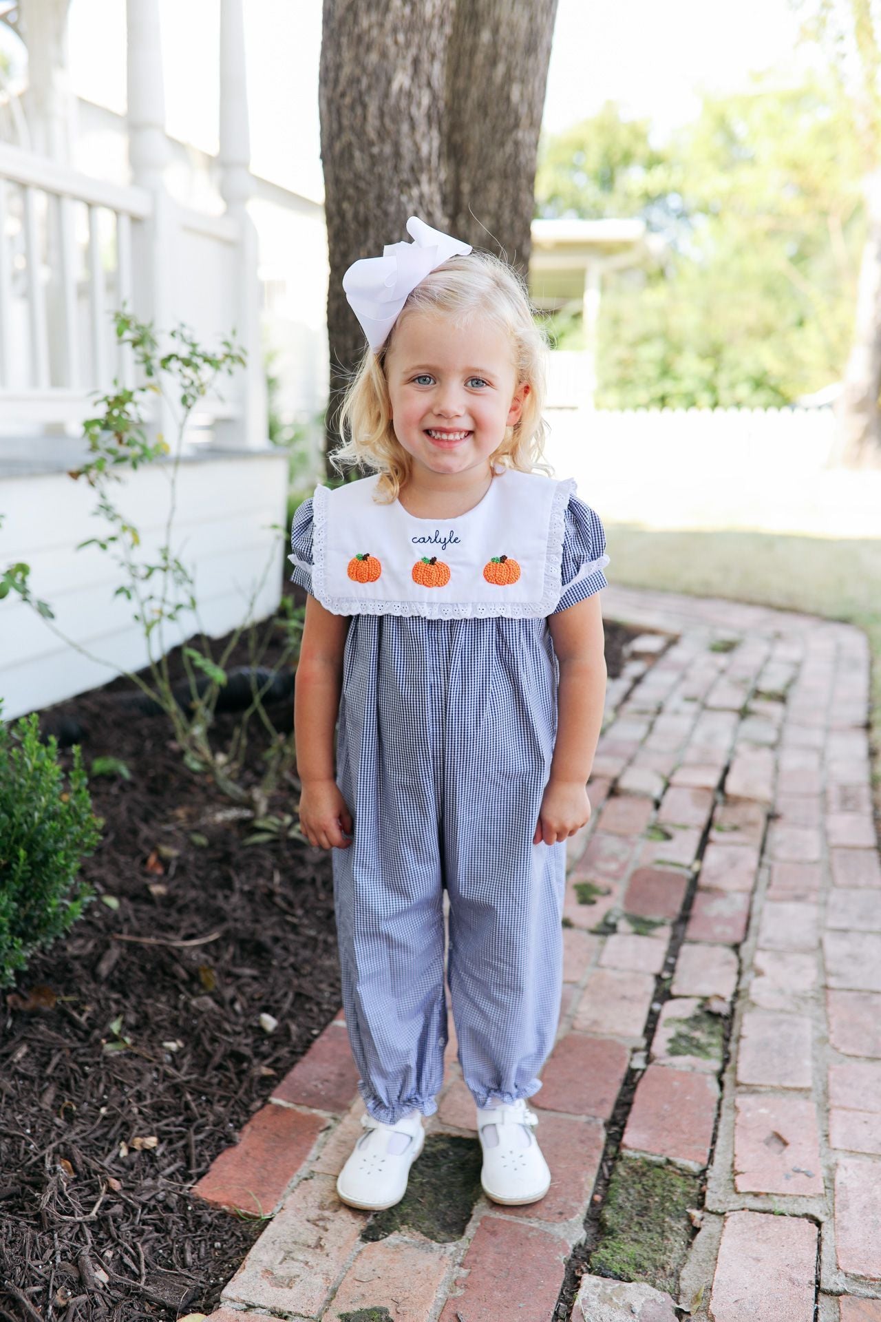 Child wearing a blue romper with pumpkin design in an outdoor setting