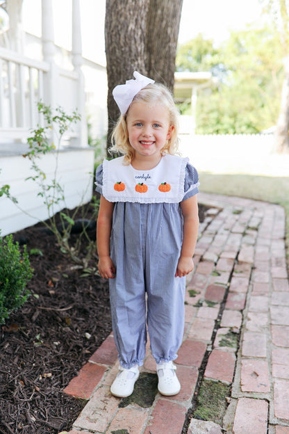 Child wearing a blue romper with pumpkin design in an outdoor setting