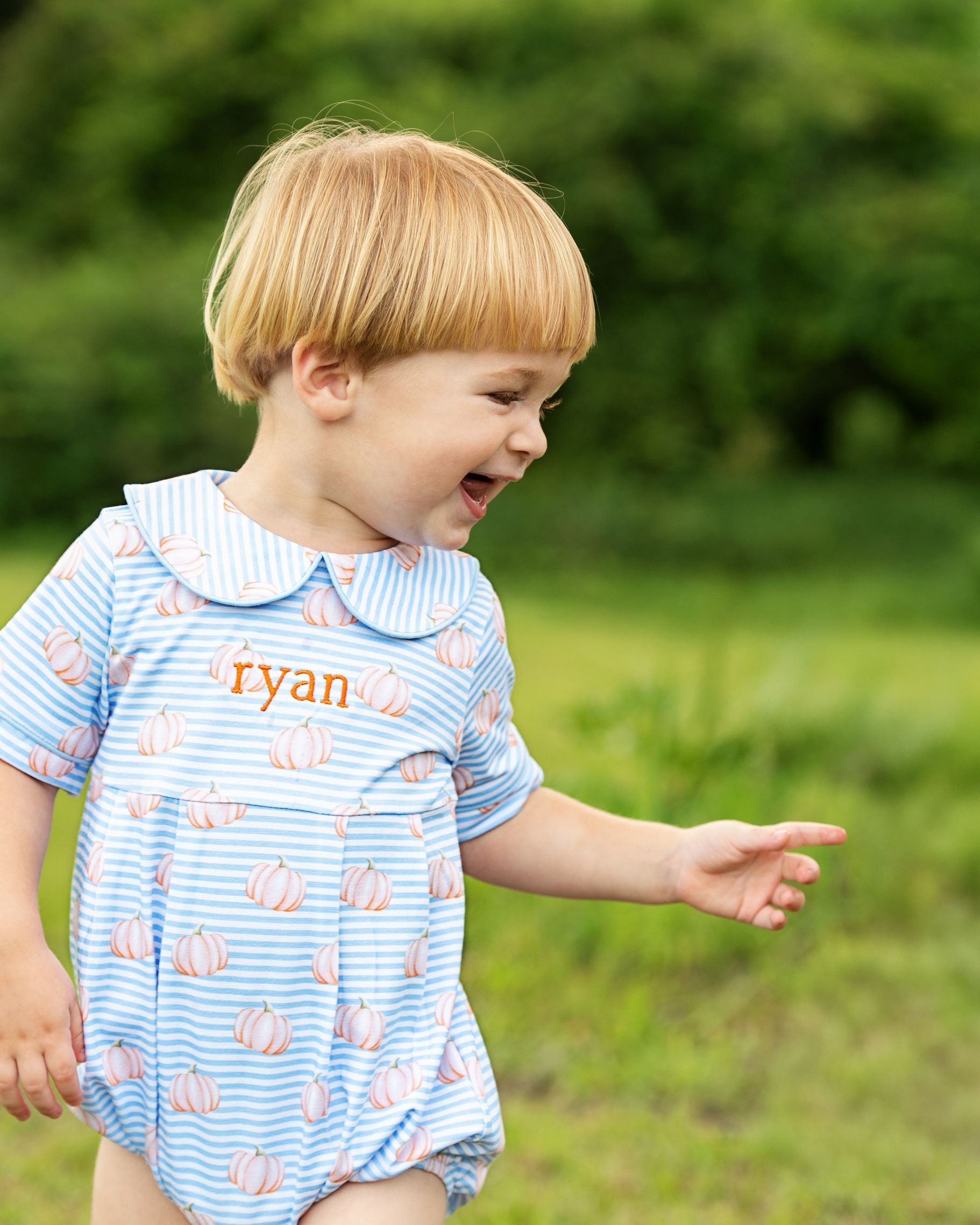 Child wearing a blue romper with pumpkin pattern outdoors
