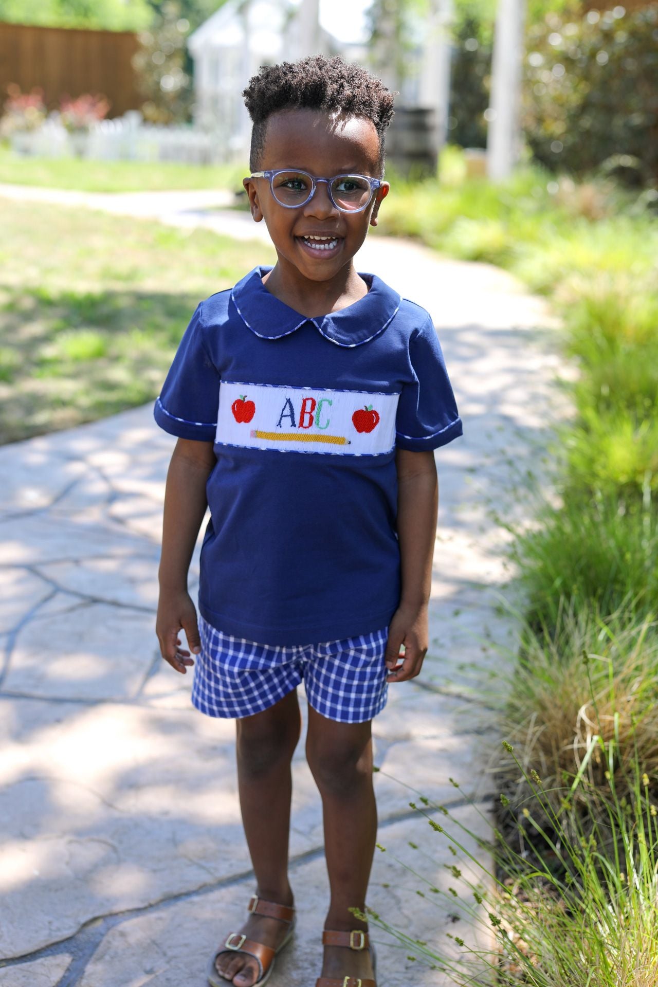 Child wearing a blue shirt with 'ABC' and apple graphics outdoors.