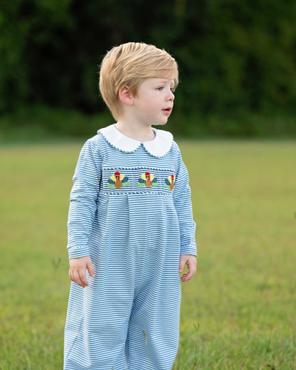 Child wearing a blue striped long romper with turkey in a grassy field 1