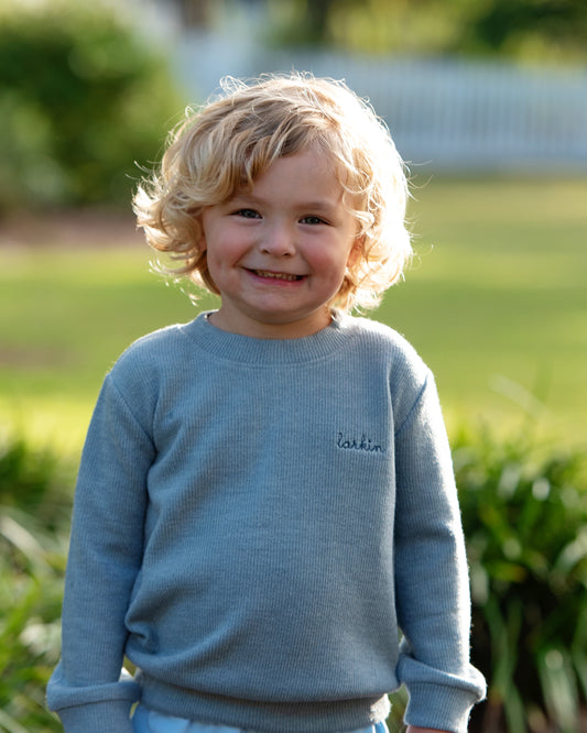 Child wearing a blue sweater with a brand logo outdoors