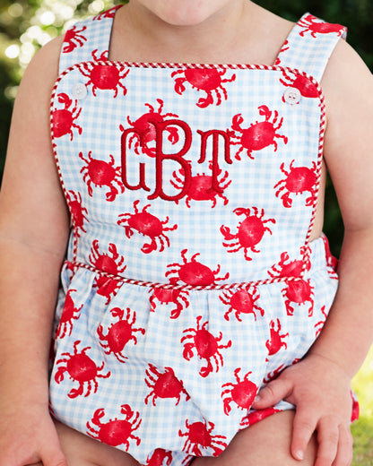 Child wearing a bubble with red crab pattern and monogram on a checkered background