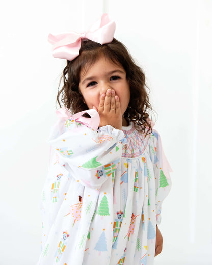 Child wearing a colorful long bubble with a holiday print and a large pink bow on a white background