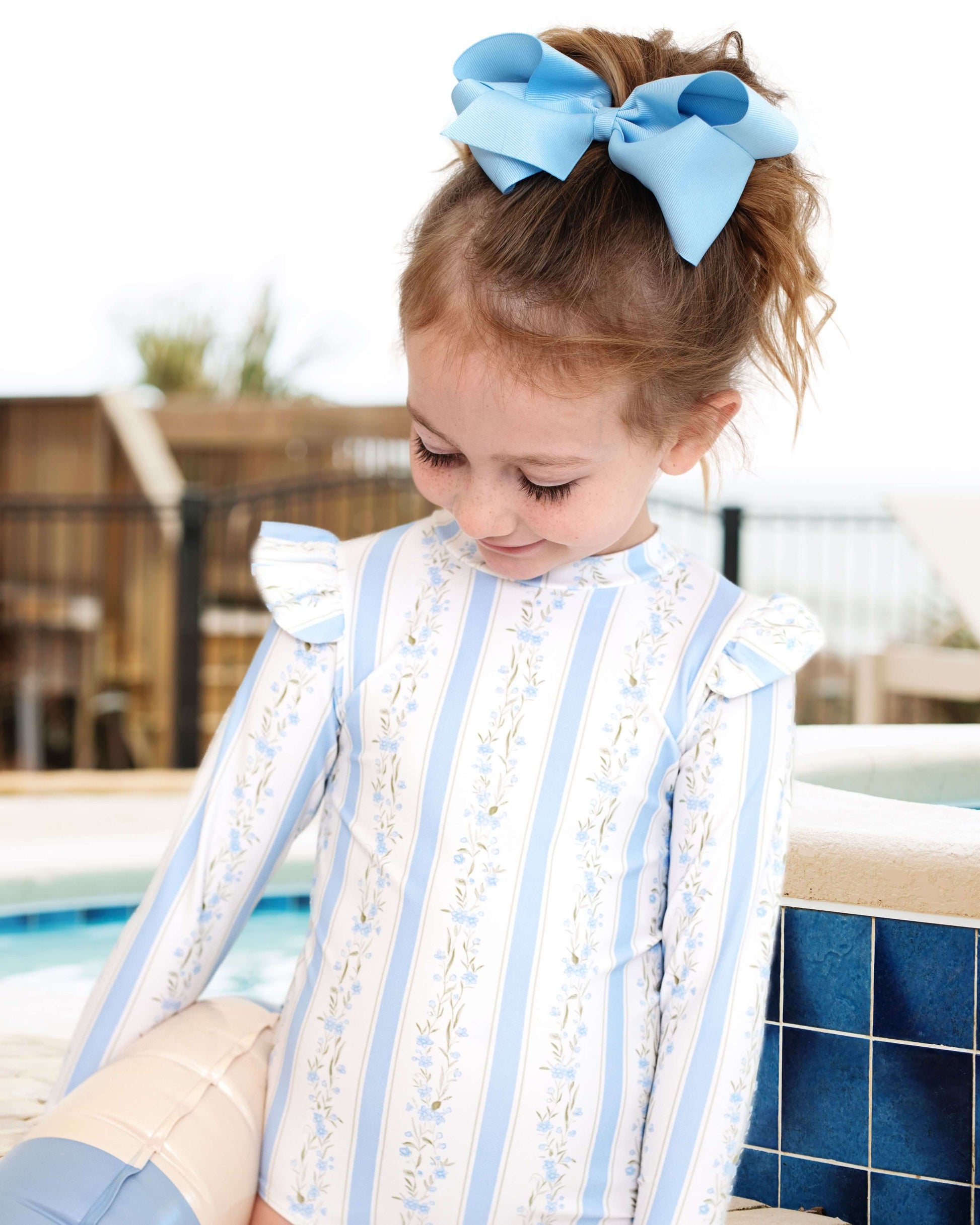 Child wearing a decorative outfit with blue ribbons by a poolside.