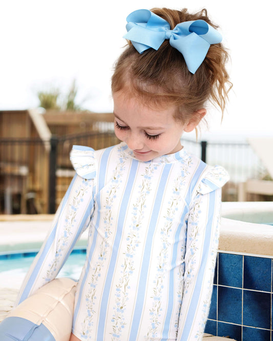 Child wearing a decorative outfit with blue ribbons by a poolside.