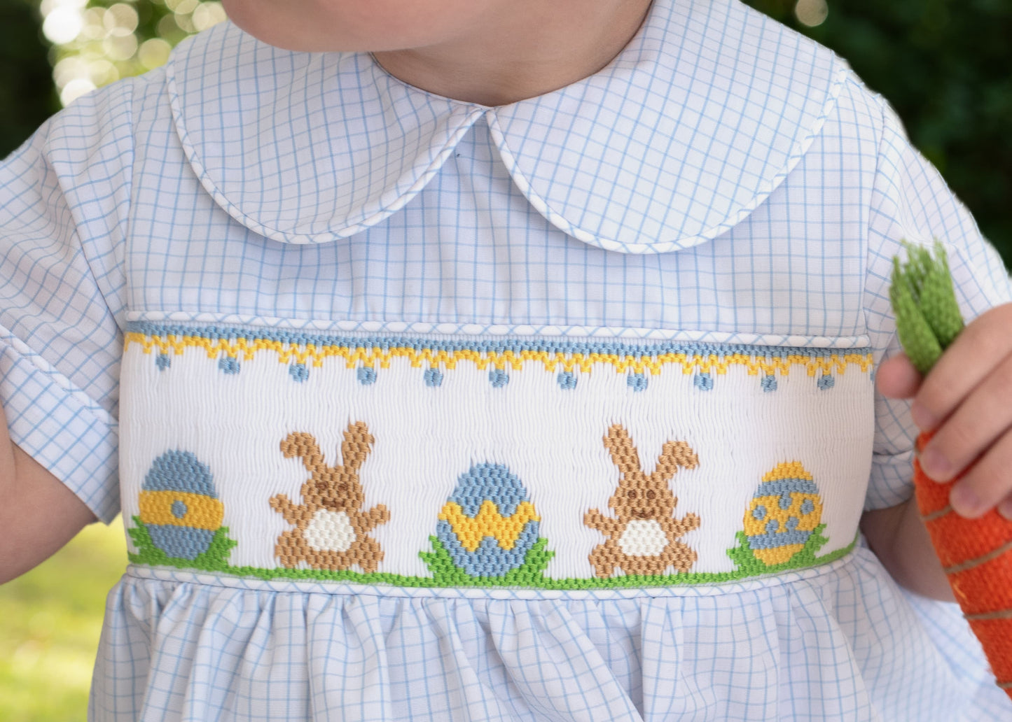 Child wearing a dress with Easter-themed embroidery of bunnies and eggs.