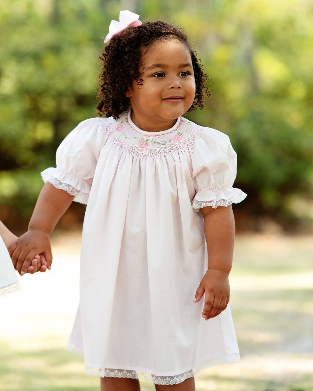 Child wearing a dress with lace details and smocking, outdoors