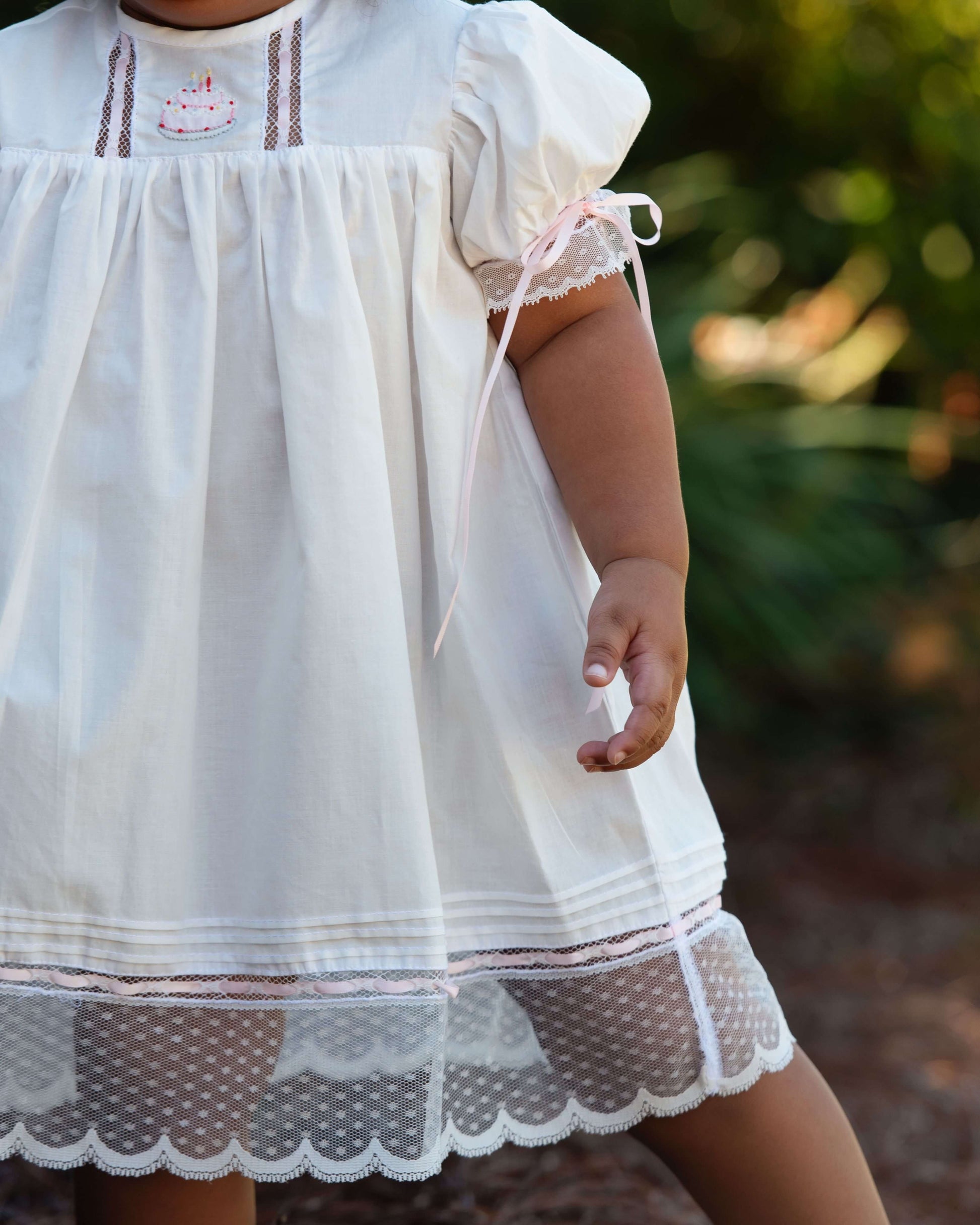 Child wearing a white dress with lace details in an outdoor setting