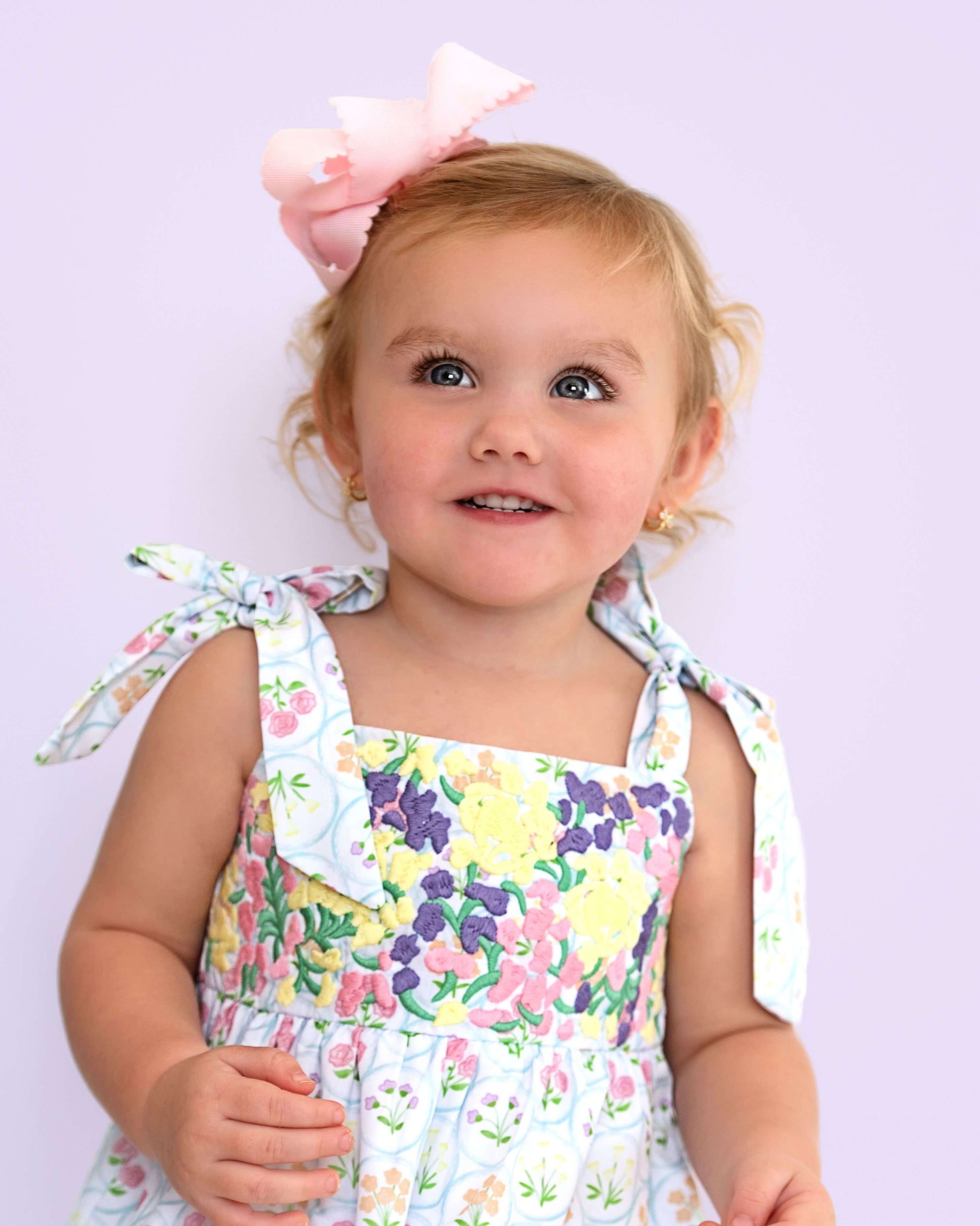 Child wearing a floral bubble with a large bow on a light purple background