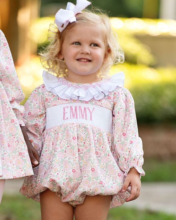 Child wearing a floral dress with 'EMMY' printed on it, standing outdoors.