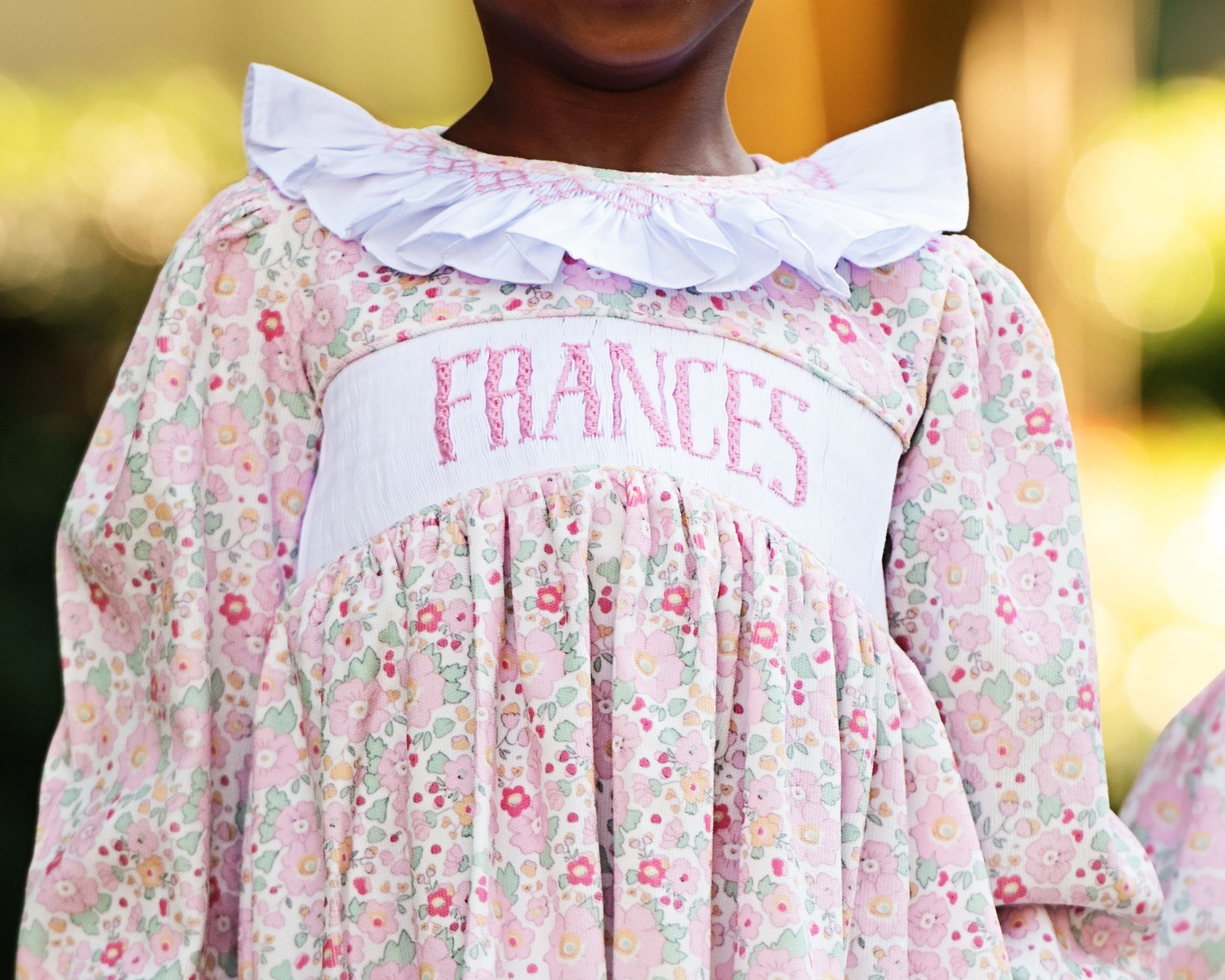 Child wearing a floral dress with 'FRANCES' embroidered on it against a blurred background