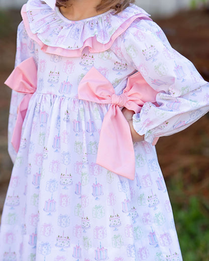 Child wearing a floral dress with a large pink bow in a natural setting