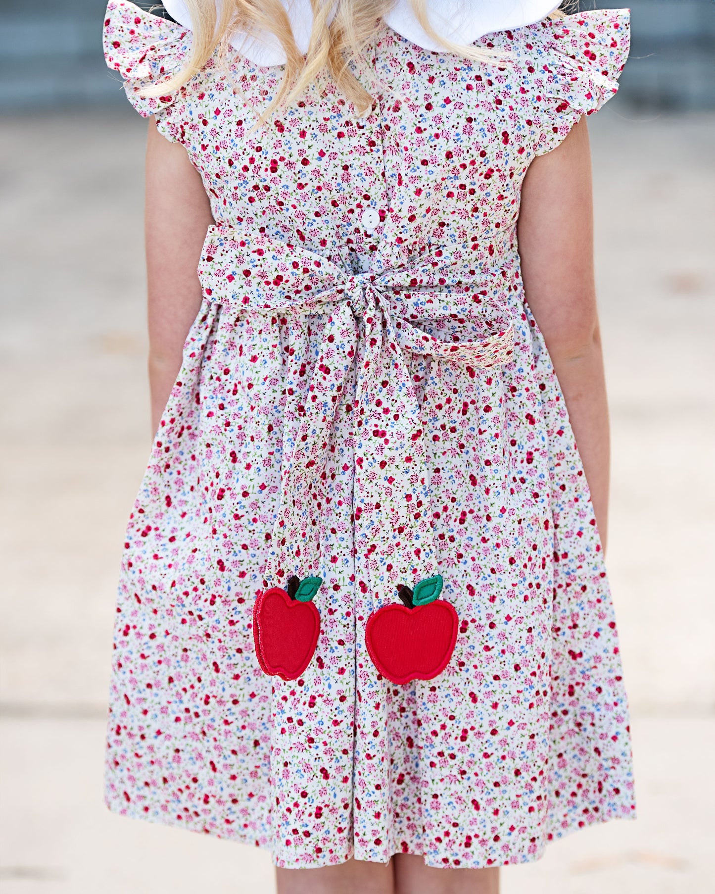 Child wearing a floral dress with red apple appliqués on a blurred background