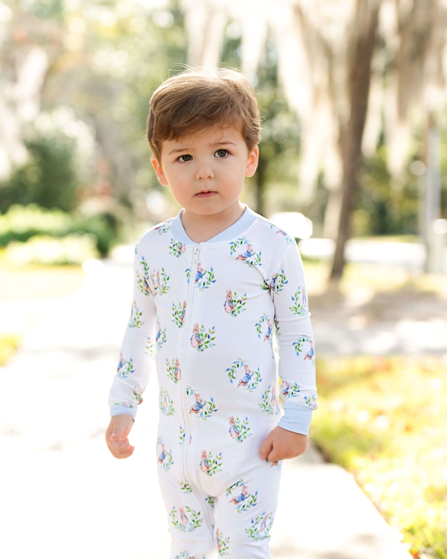 Child wearing a floral onesie standing outdoors with trees and grass in the background