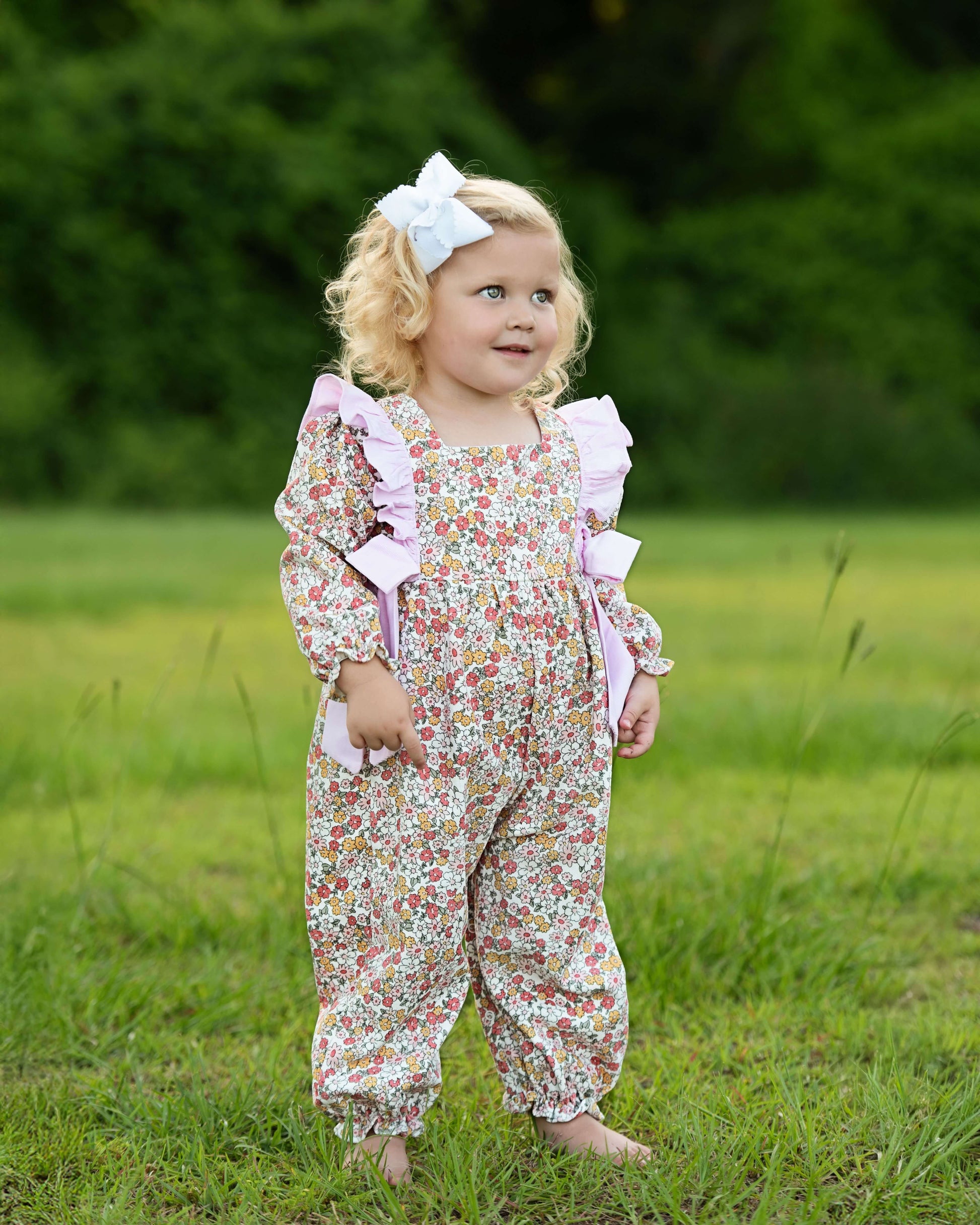 Child wearing a floral outfit with ruffles standing in a grassy field