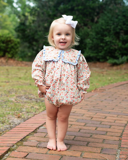 Child wearing a floral romper with a bow in a garden setting
