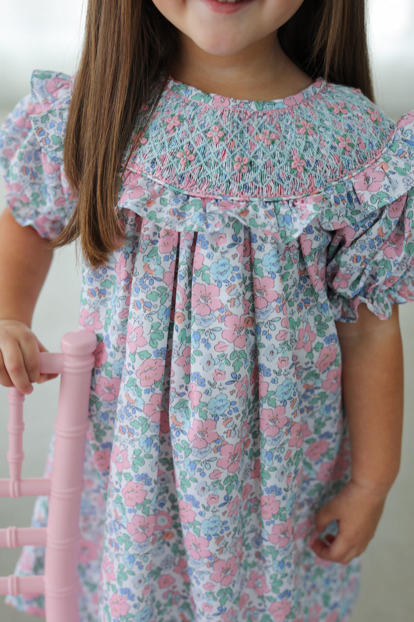 Child wearing a floral smocked dress holding a pink chair.
