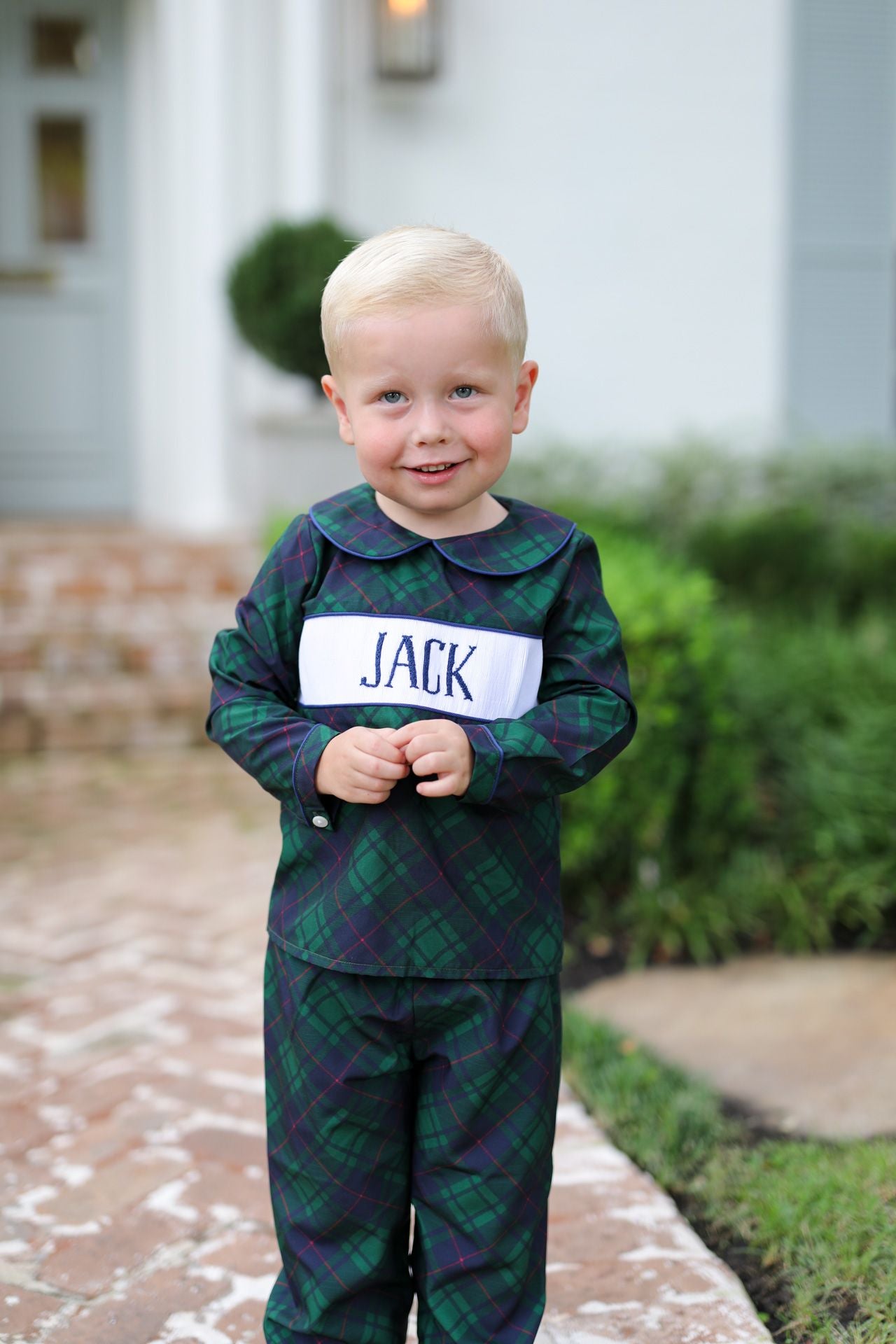Child wearing a green plaid outfit with a name tag outdoors.