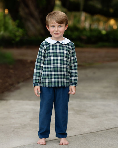 Child wearing a green plaid shirt with a white collar and blue pants standing on a sidewalk.