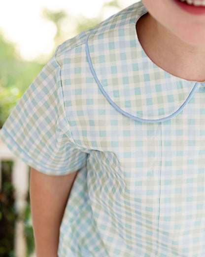 Child wearing a light blue and white checkered dress with a blurred outdoor background