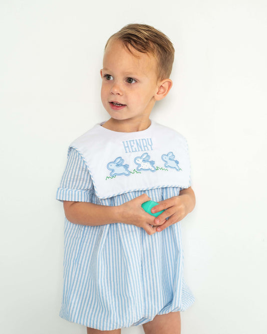 Child wearing a light blue and white striped bubble with embroidered design on a plain background
