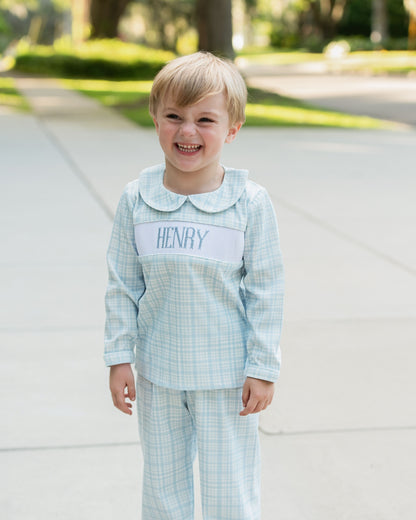 Child wearing a light blue checkered outfit with a name label outdoors.