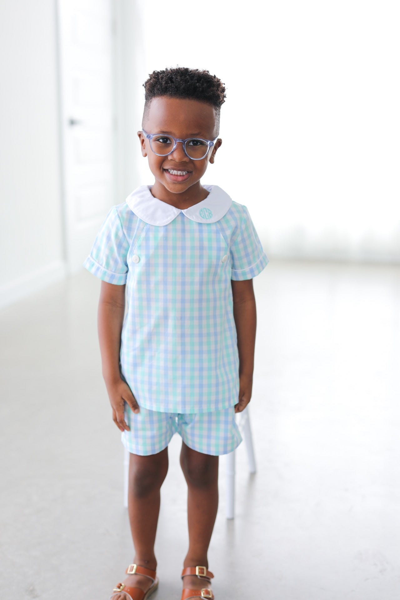 Child wearing a light blue checkered outfit with a white collar on a white background