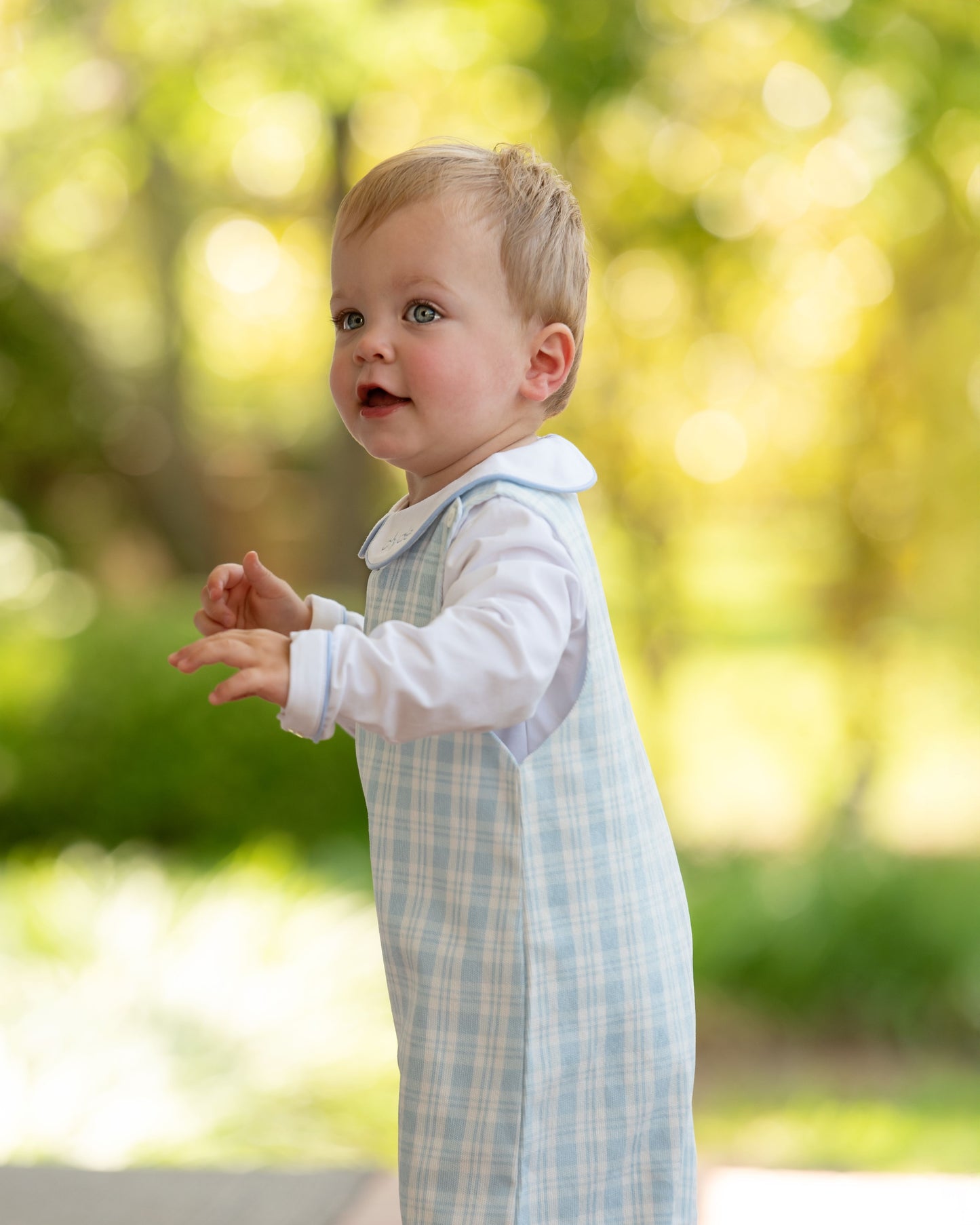 Child wearing a light blue checkered outfit with a white shirt outdoors.