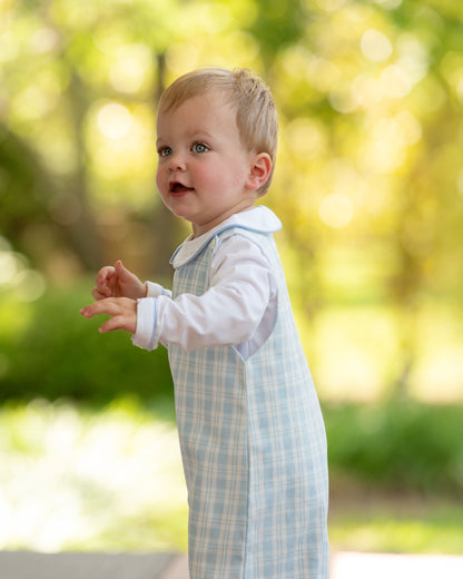 Child wearing a light blue checkered outfit with a white shirt outdoors.