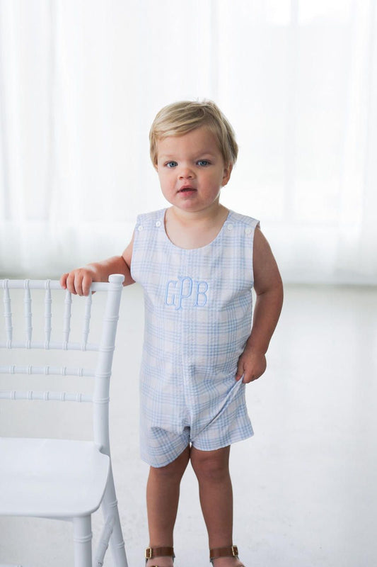 Child wearing a light blue checkered romper with 'Daddy' printed on it, standing against a white background.