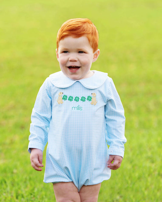 Child wearing a light blue checkered romper with embroidered design on a grassy background