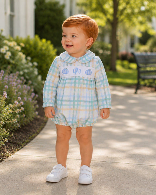 Child wearing a light blue checkered romper with white sneakers in a garden setting