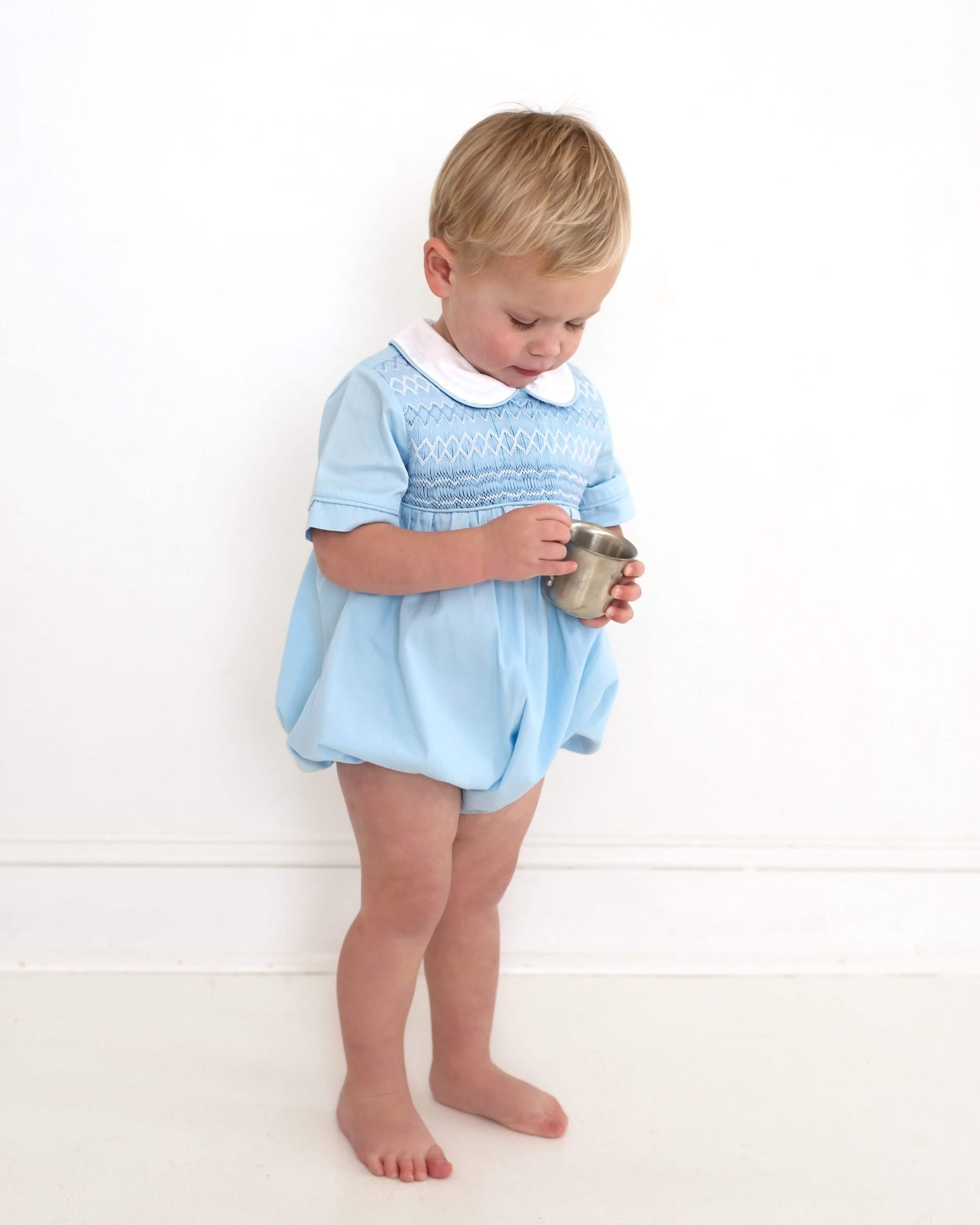 Child wearing a light blue dress holding a small cup on a white background
