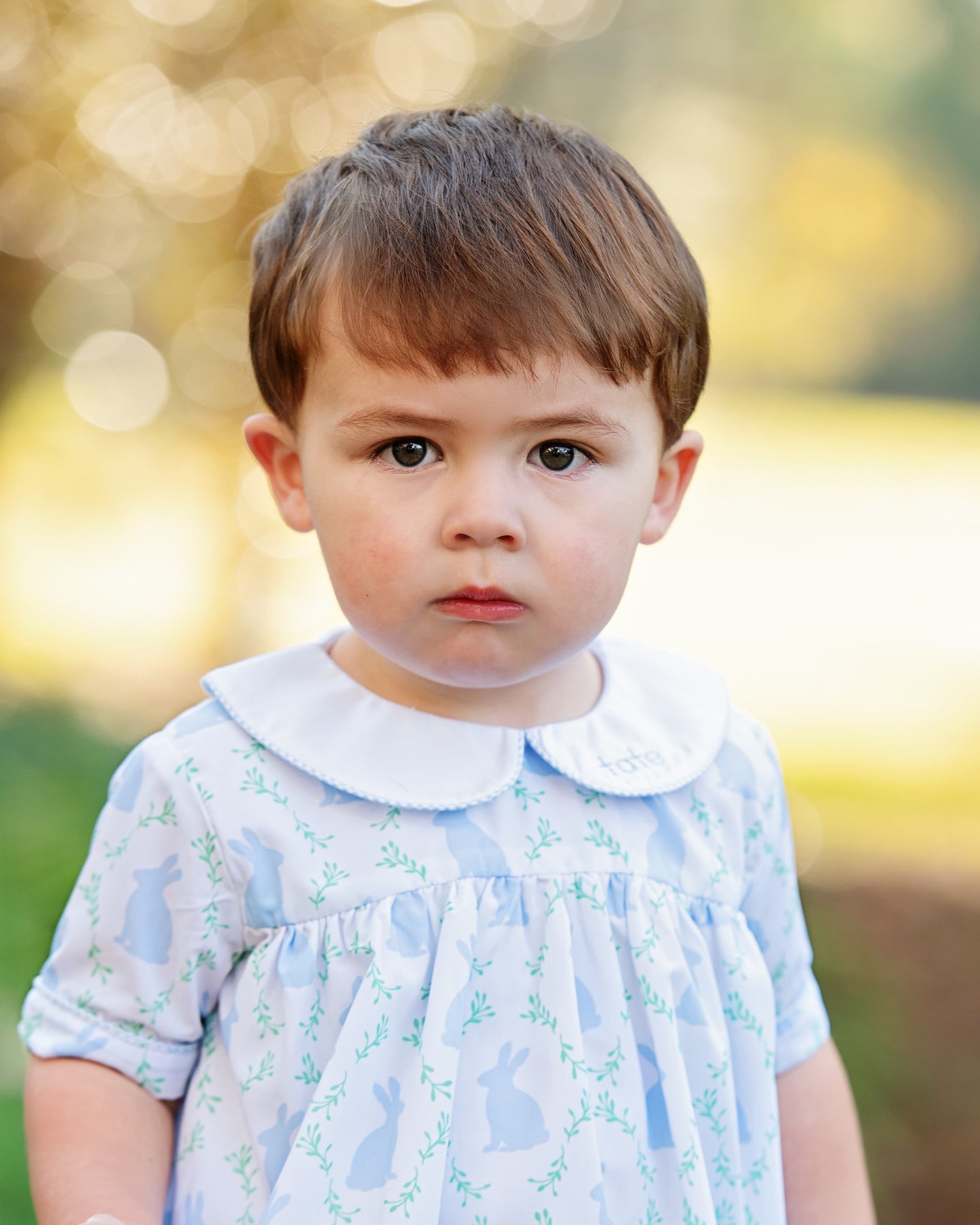 Child wearing a light blue dress with a white collar against a blurred natural background