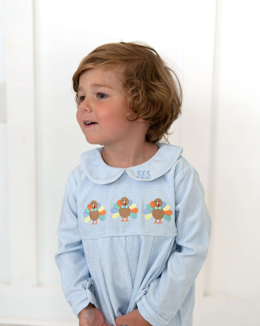 Young boy wearing a blue gingham embroidered turkey romper for Thanksgiving