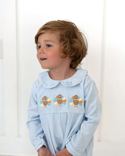 Child wearing a light blue dress with embroidered turkeys on a white background