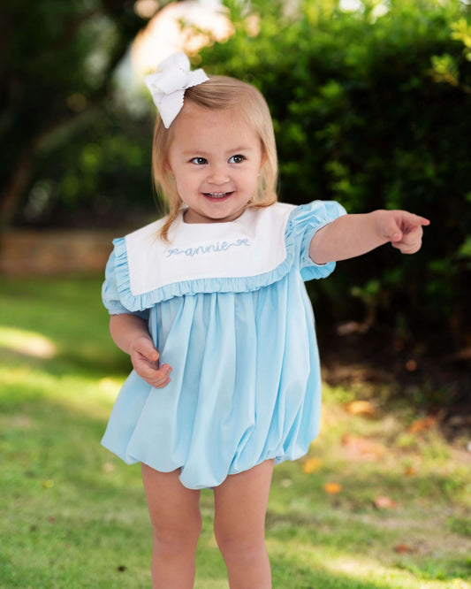 Child wearing a light blue dress with white trim outdoors