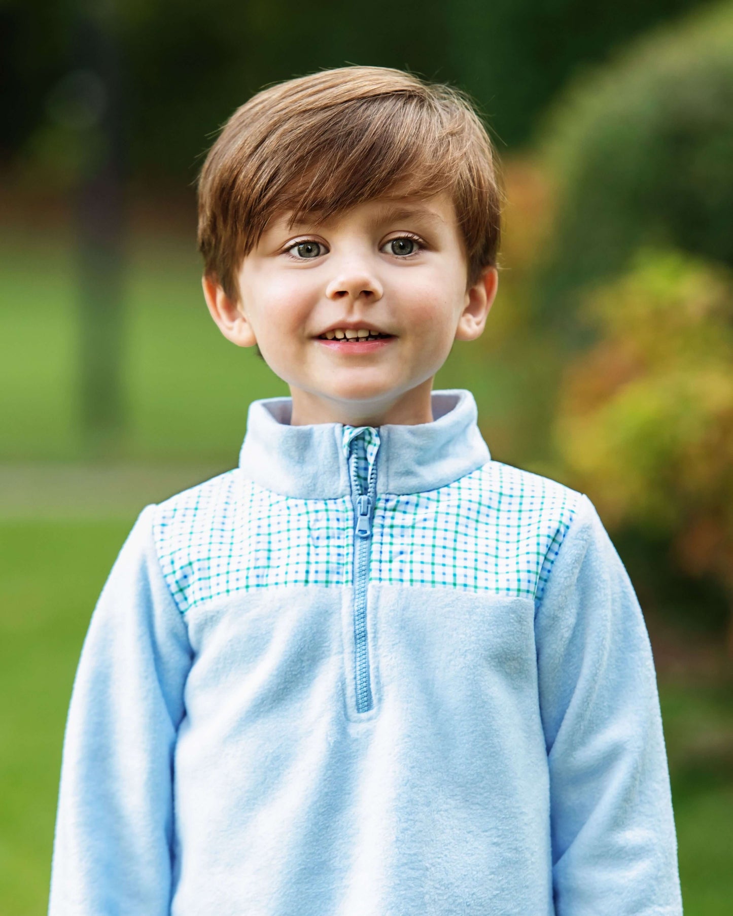 Child wearing a light blue fleece jacket with a checkered pattern on a blurred green background