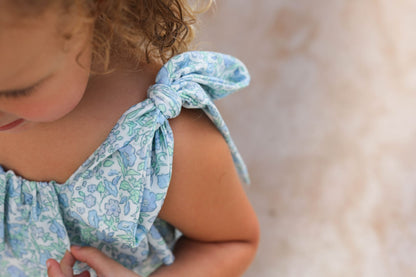 Child wearing a light blue floral dress with a bow detail on a blurred background