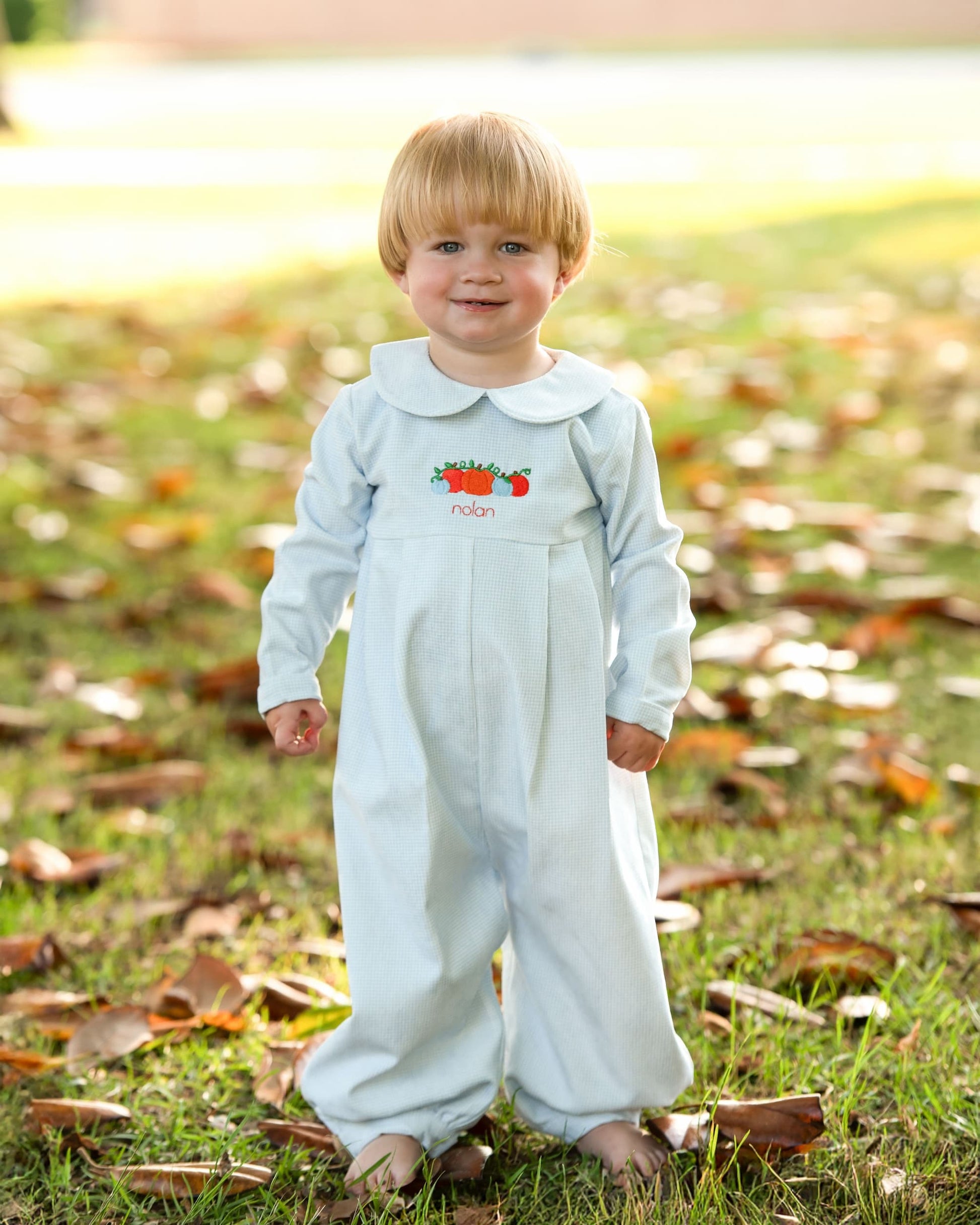 Child wearing a light blue long romper with a design in a grassy outdoor setting