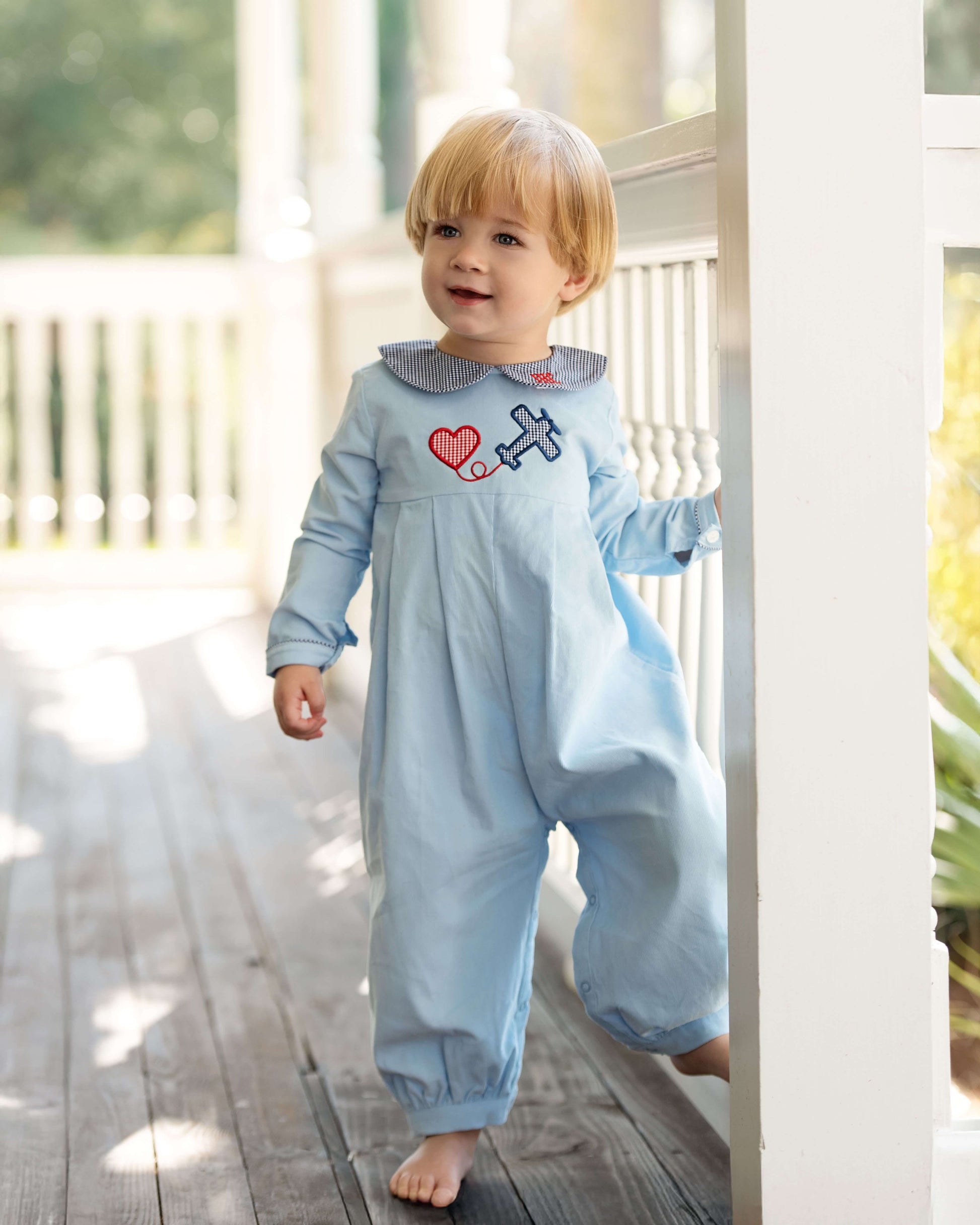 Child wearing a light blue onesie with a heart and airplane design on a wooden deck.