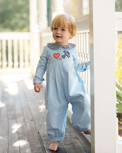 Child wearing a light blue onesie with a heart and airplane design on a wooden deck.