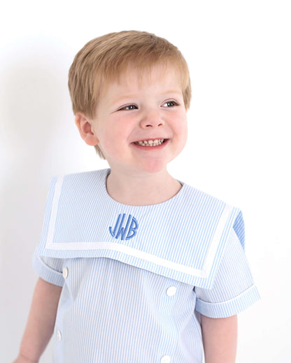 Child wearing a light blue outfit with a monogrammed square collar over shoulders against a white background