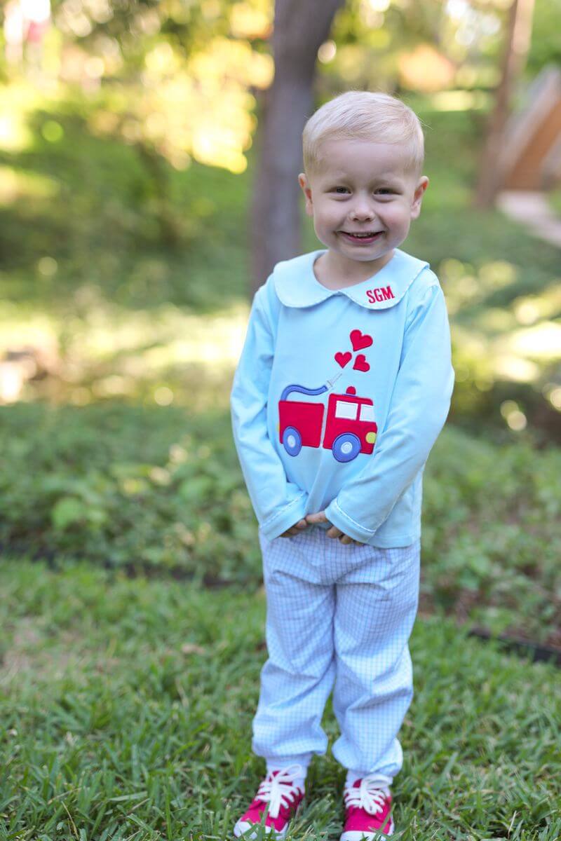 Child wearing a light blue outfit with a red fire truck design outdoors.
