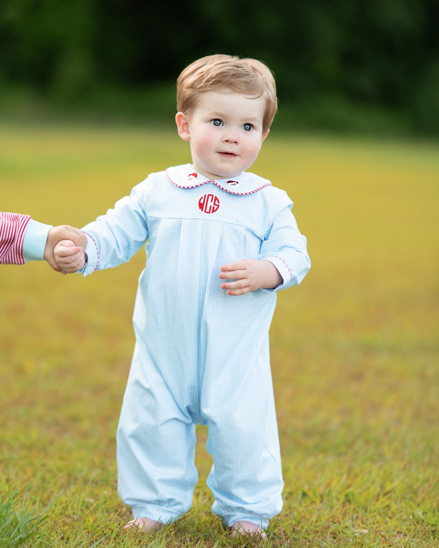 Child wearing a light blue outfit with a red monogram in a grassy field